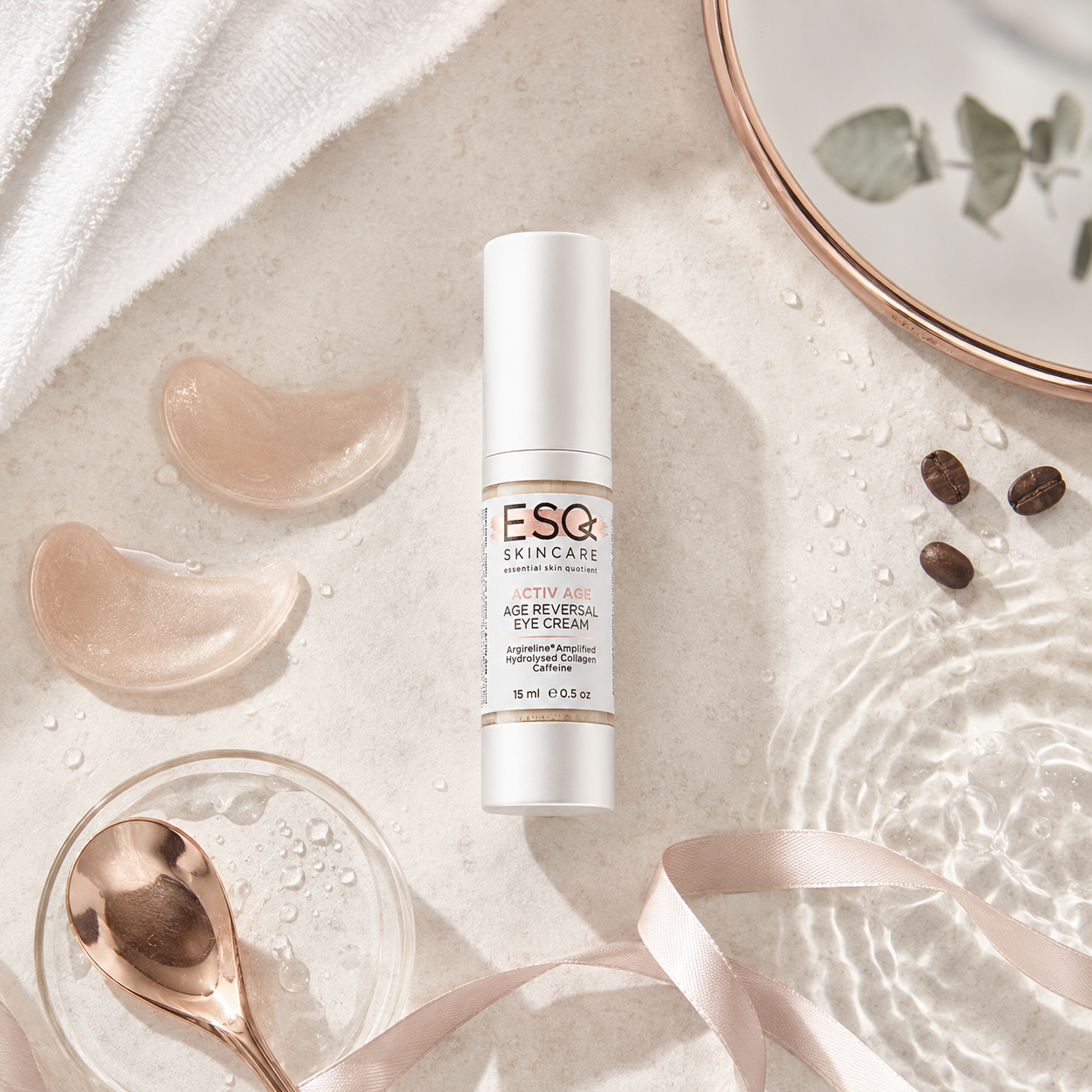 A skincare product bottle labeled ESC SkinCare Age Reversing Eye Cream, styled in a flat-lay arrangement with a white towel, translucent gel patches, a rose gold spoon, and water droplets on a light stone surface.
