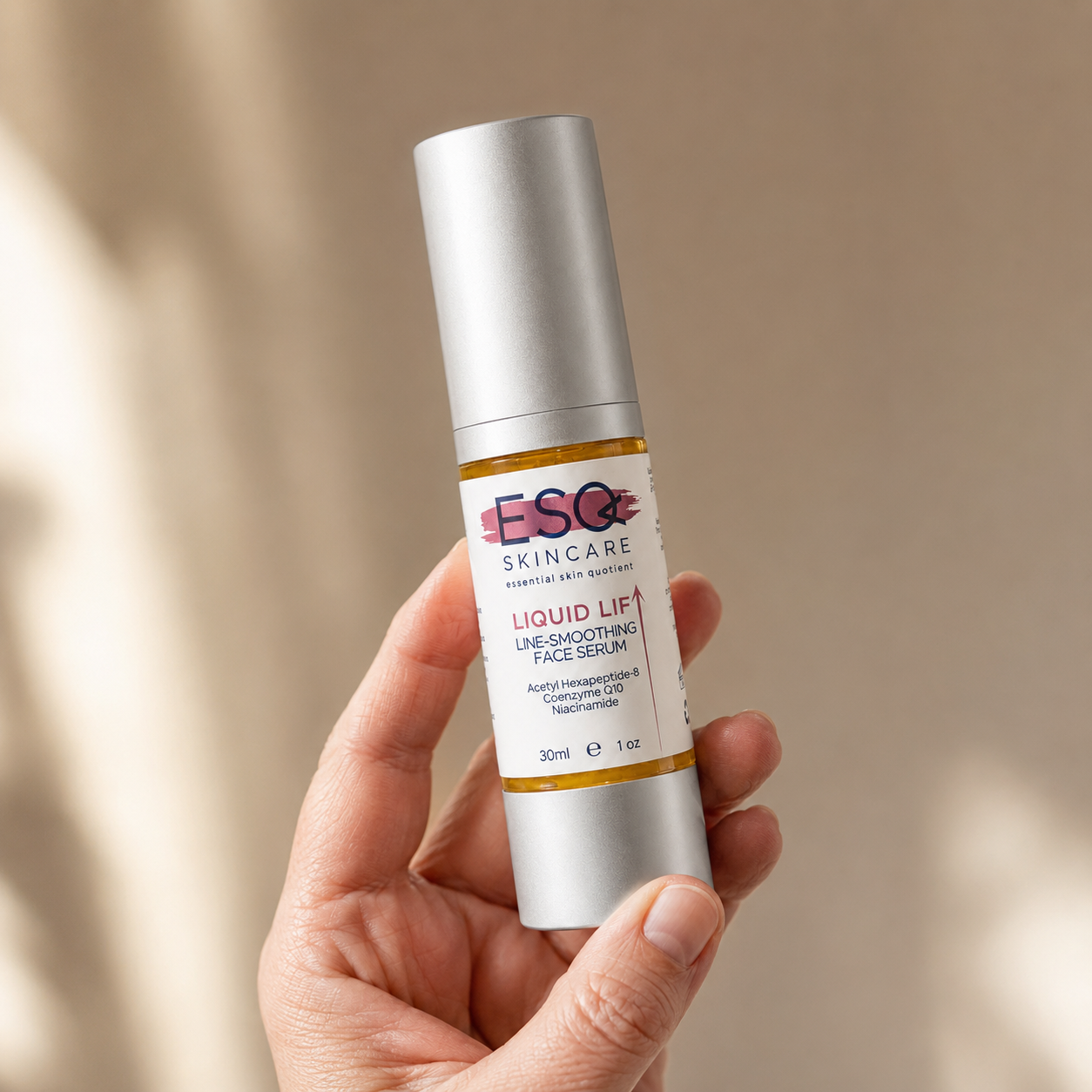 A hand holding a silver bottle of ESQ Skincare Liquid Lift Line-Smoother Face Serum against a warm beige background with soft shadows.