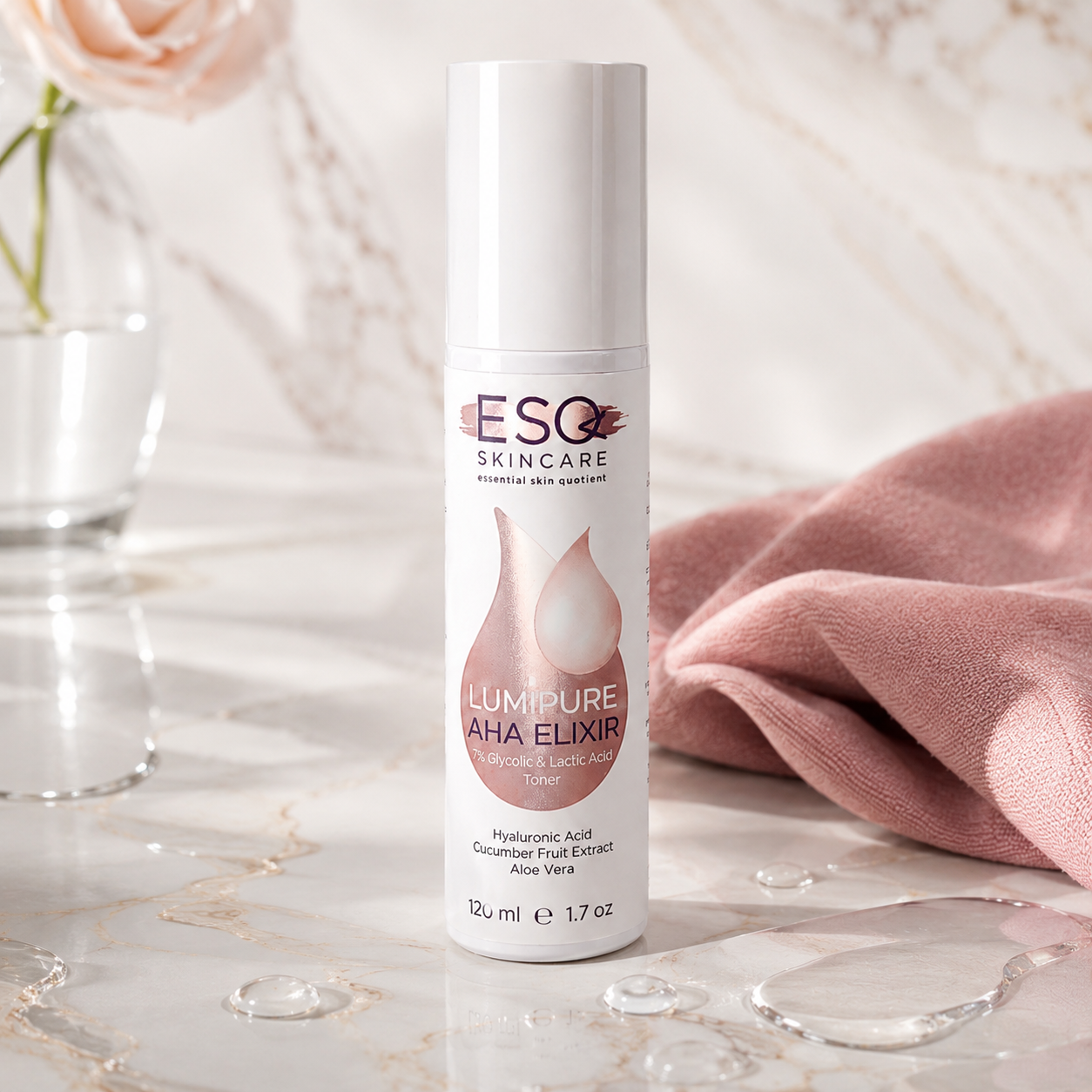 A 120 ml bottle of ESQ Skincare 'Lumipure AHA Elixir' stands on a polished marble surface, flanked by a soft pink cloth and a glass vase with a rose.