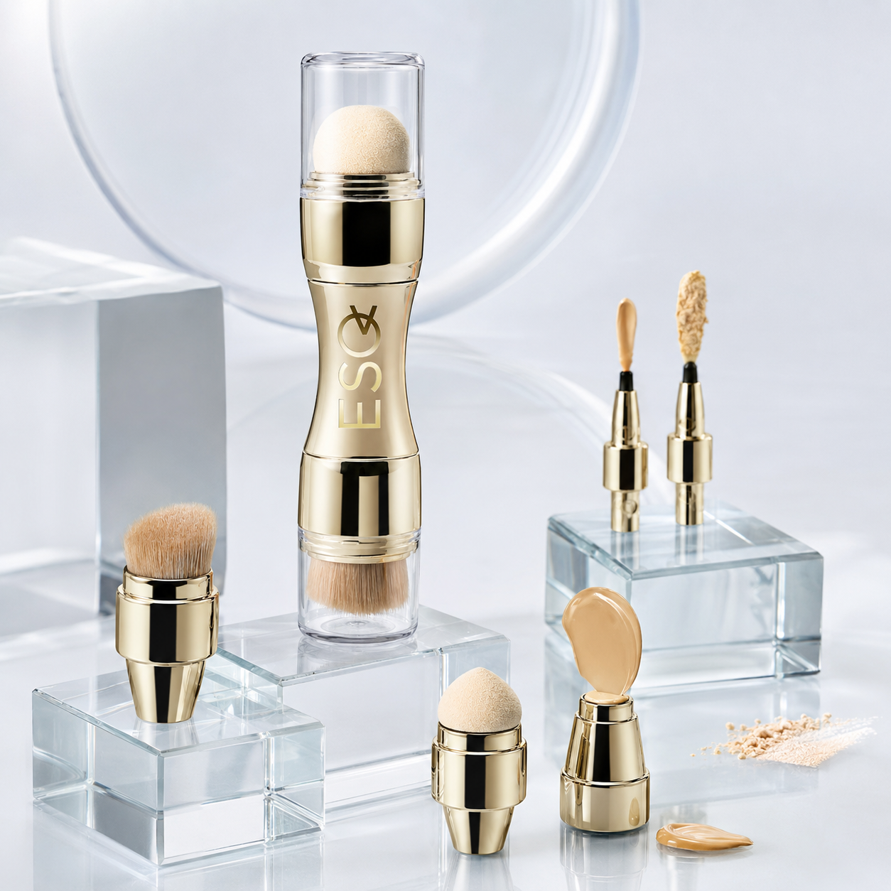 A set of gold and clear cosmetic applicators and brushes displayed on transparent acrylic blocks against a soft white studio background. The products include a dual-ended makeup stick with a clear cap, several brush tips, sponge-like applicators, and small makeup swatches.