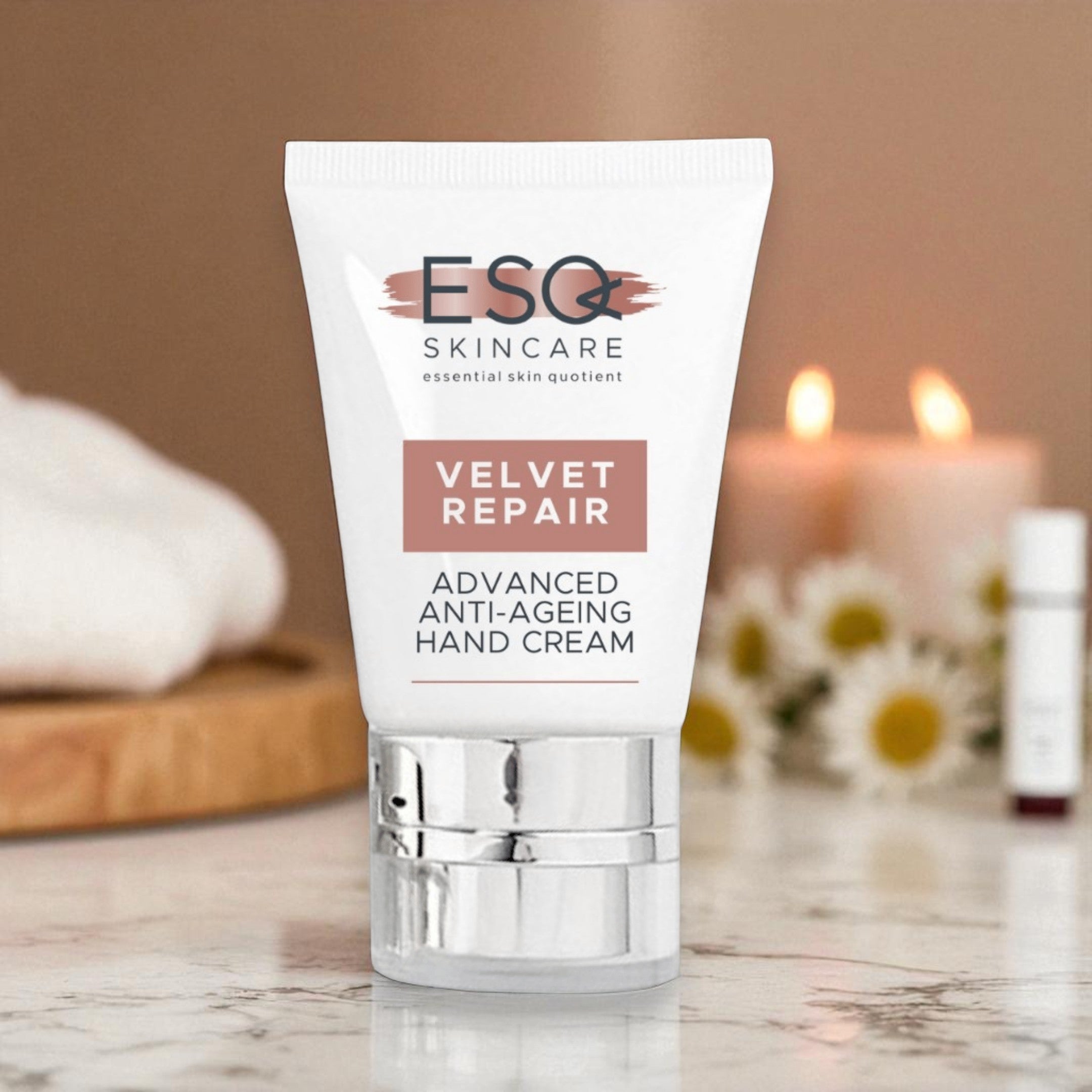Tube of ESQ Skincare Velvet Repair hand cream on a marble surface with candles and flowers in the background.