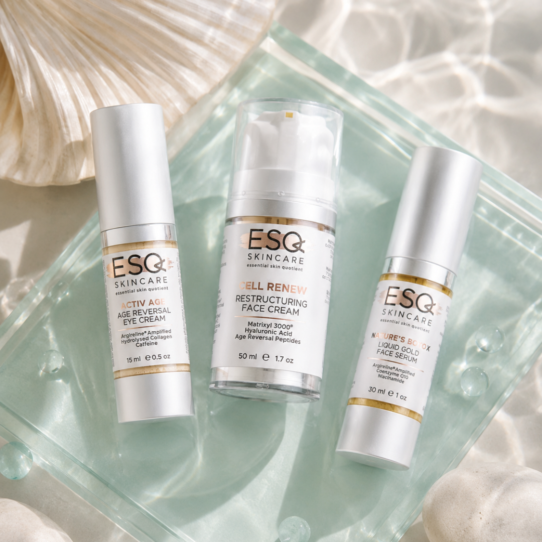 Three ESQ Skincare skincare bottles arranged on a translucent glass tray with soft white fabric and shell props. The products are: Activ Age Age Reversal Eye Cream, Cell Renew Restructuring Face Cream, and Cell Renew Liquid Silk Facial Serum.